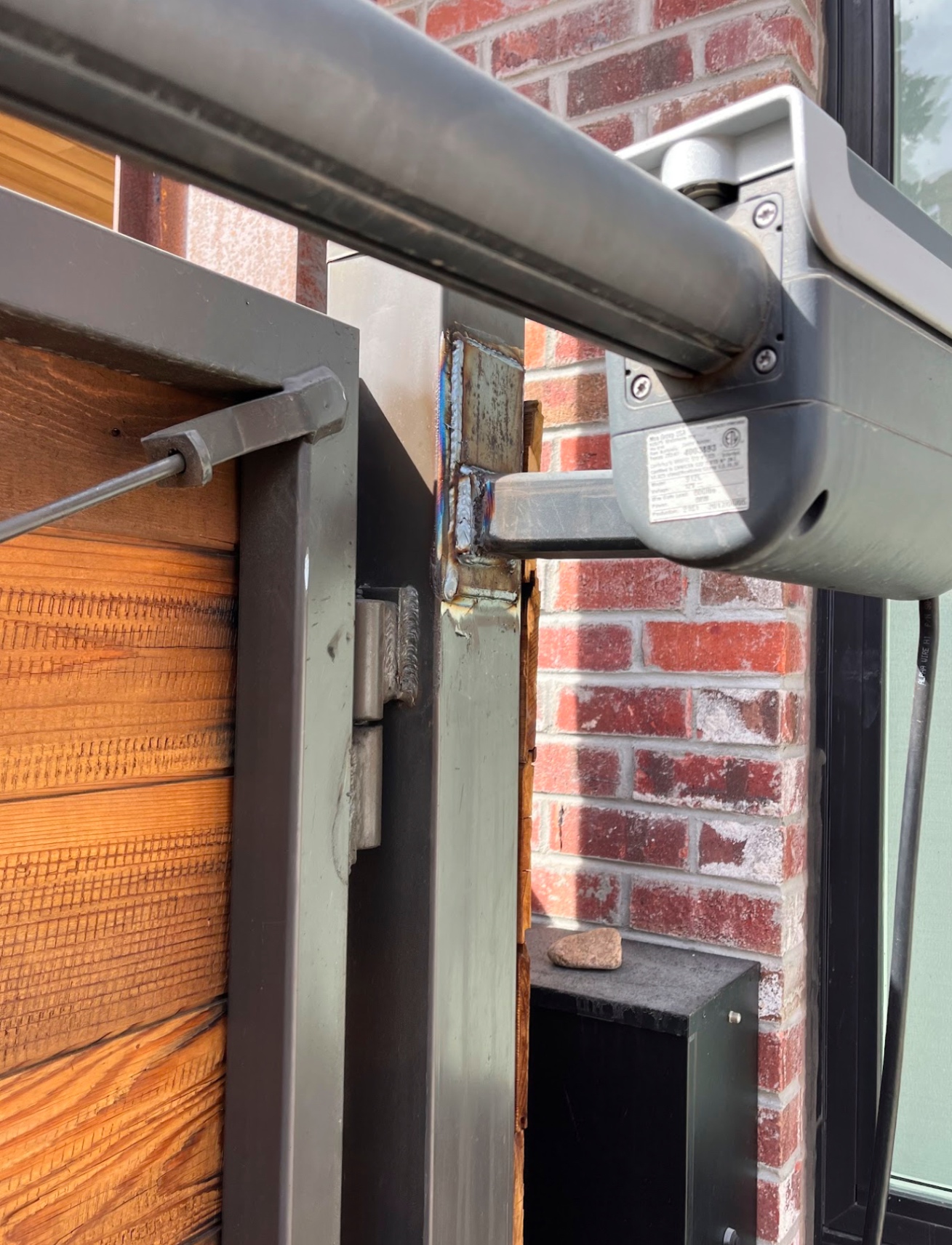 Automated swing gate opener arm welded to steel gate frame at brick home