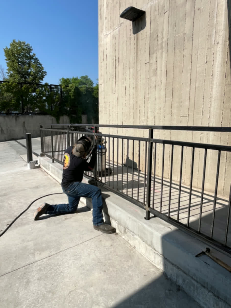 Welder installing black steel safety railing on commercial concrete ramp