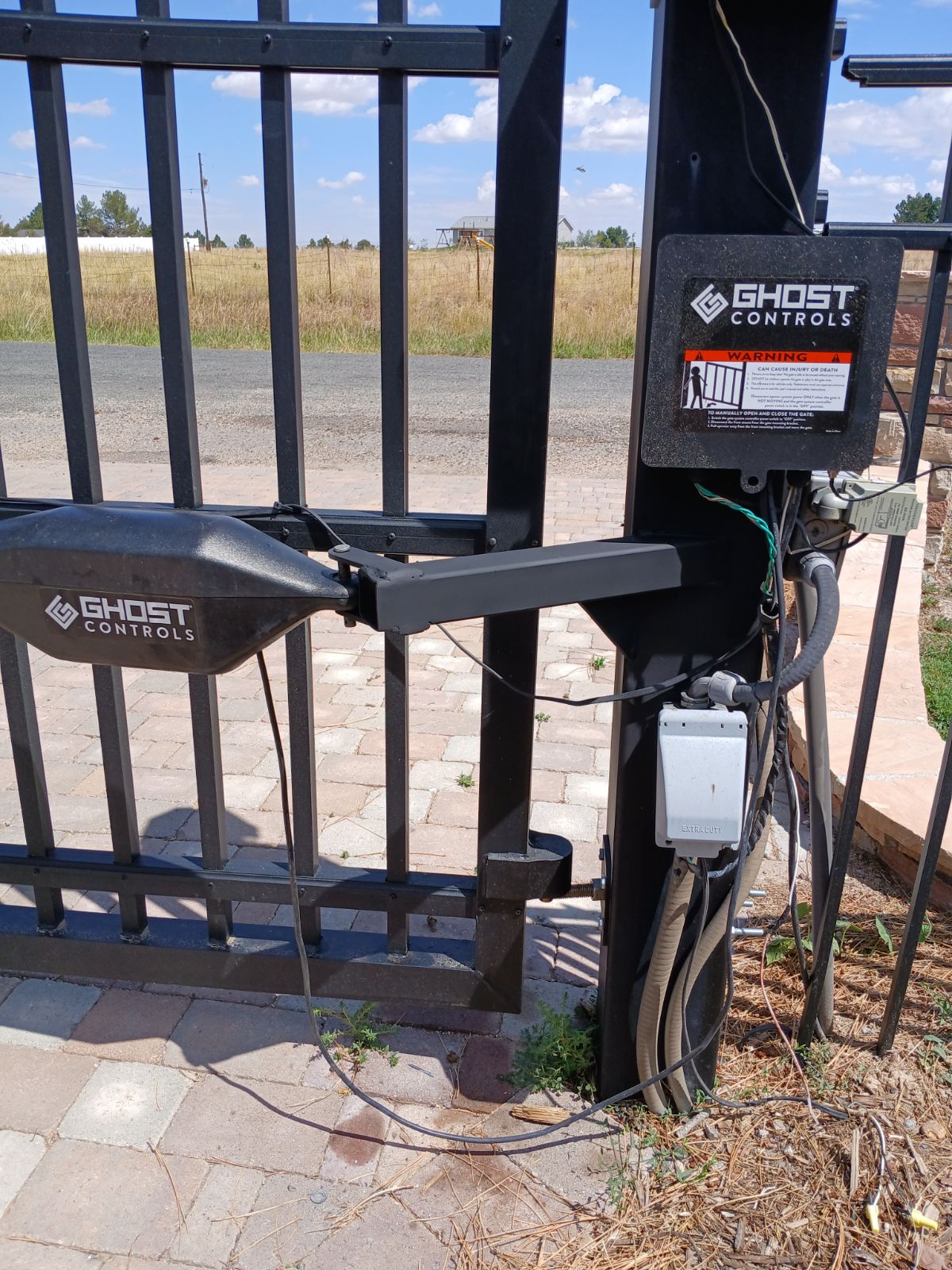 Automated Ghost Controls opener on black steel driveway gate