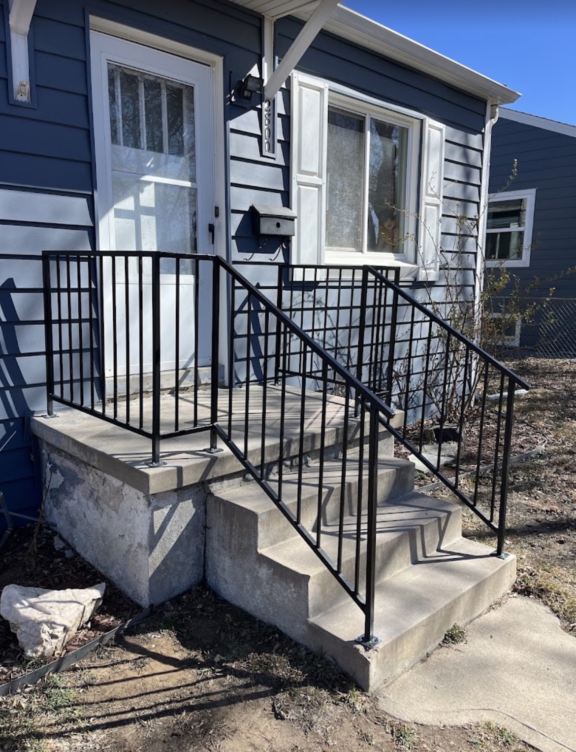 Black steel step railings on blue bungalow entry